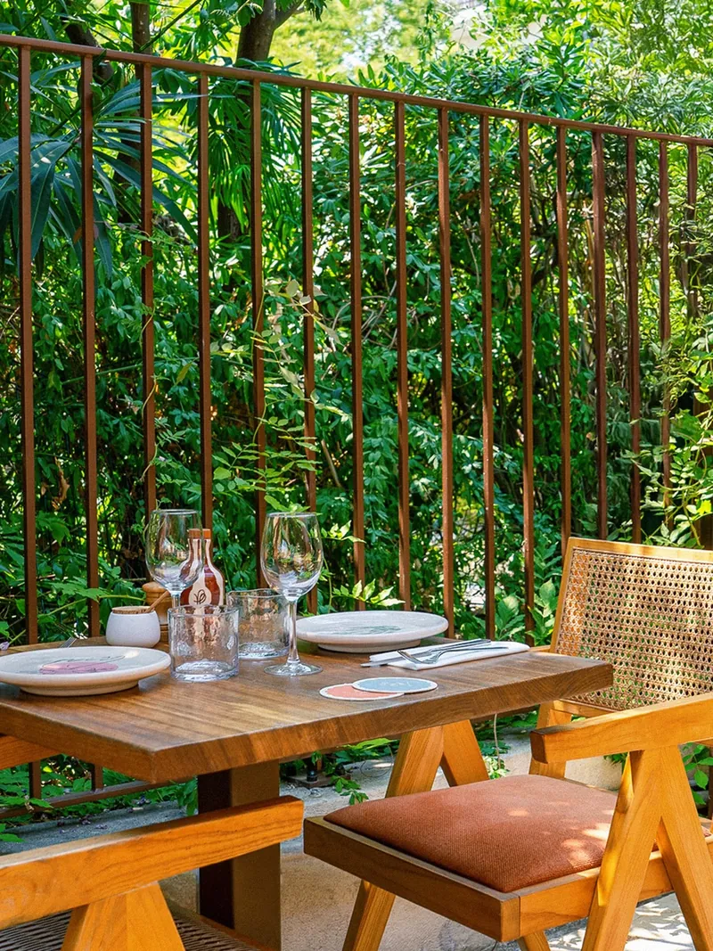 La terrasse du patio, tables en bois et chaises cannées sous la verdure